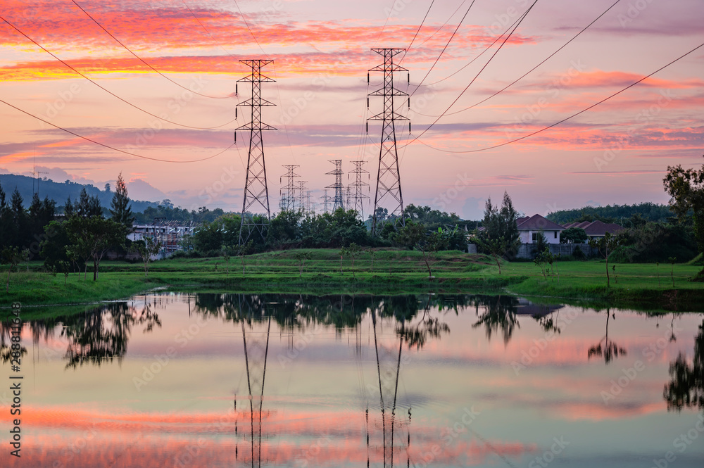 View before sunset with beautiful clouds and sun before the horizon. There are high voltage electricity poles and cables. Reflection from the lake water