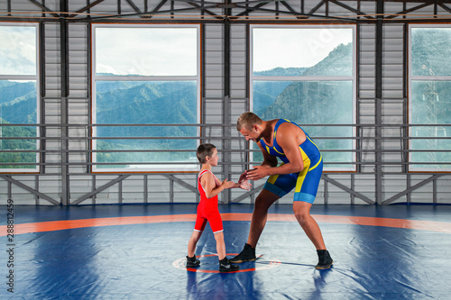 An adult male wrestler coach teaches the basics of wrestling and sets up a little boy to compete. The concept of child power and martial arts training. Teaching children Greco-Roman wrestling photo