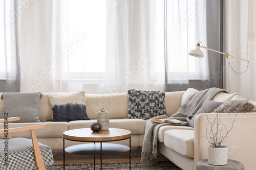 Beige comfortable corner sofa with grey pillows in elegant living room interior with white wall