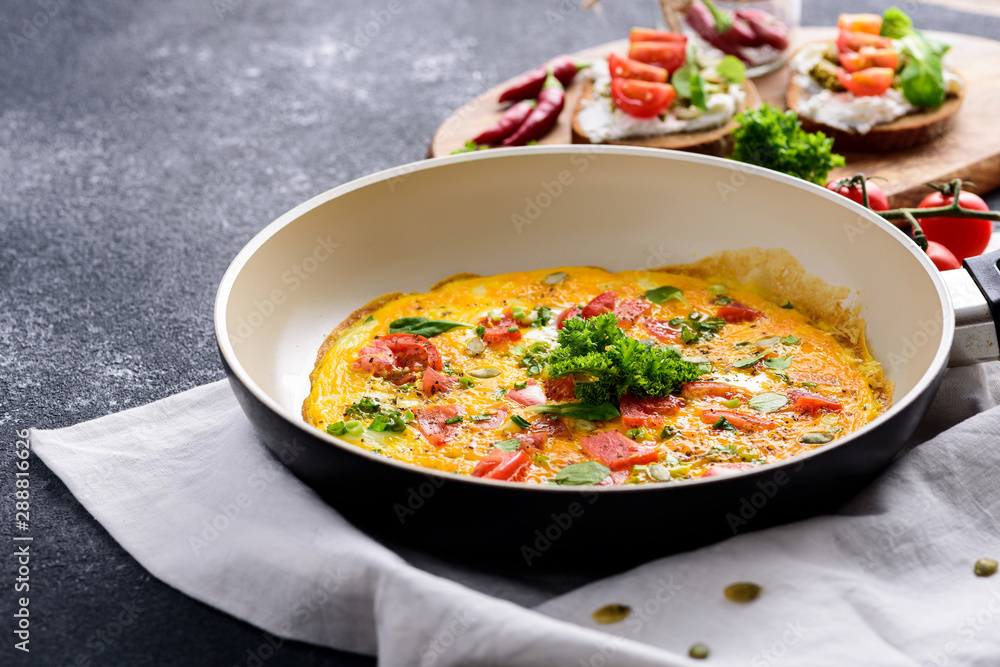 omelette in a frying pan with tomatoes and greens on a dark background, healthy vegan Breakfast