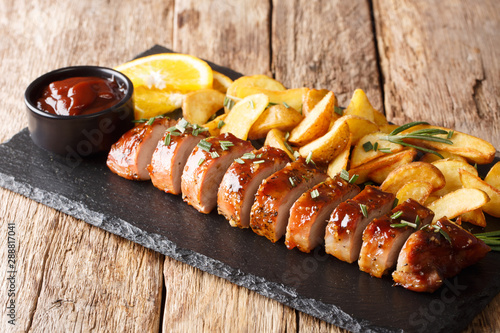 Fotografija Traditional baked pork tenderloin with potato wedges close-up on a slate board