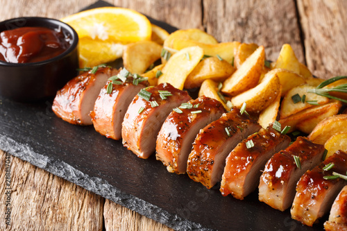 Tasty glazed pork tenderloin with potato wedges close-up on a slate board on the table. horizontal