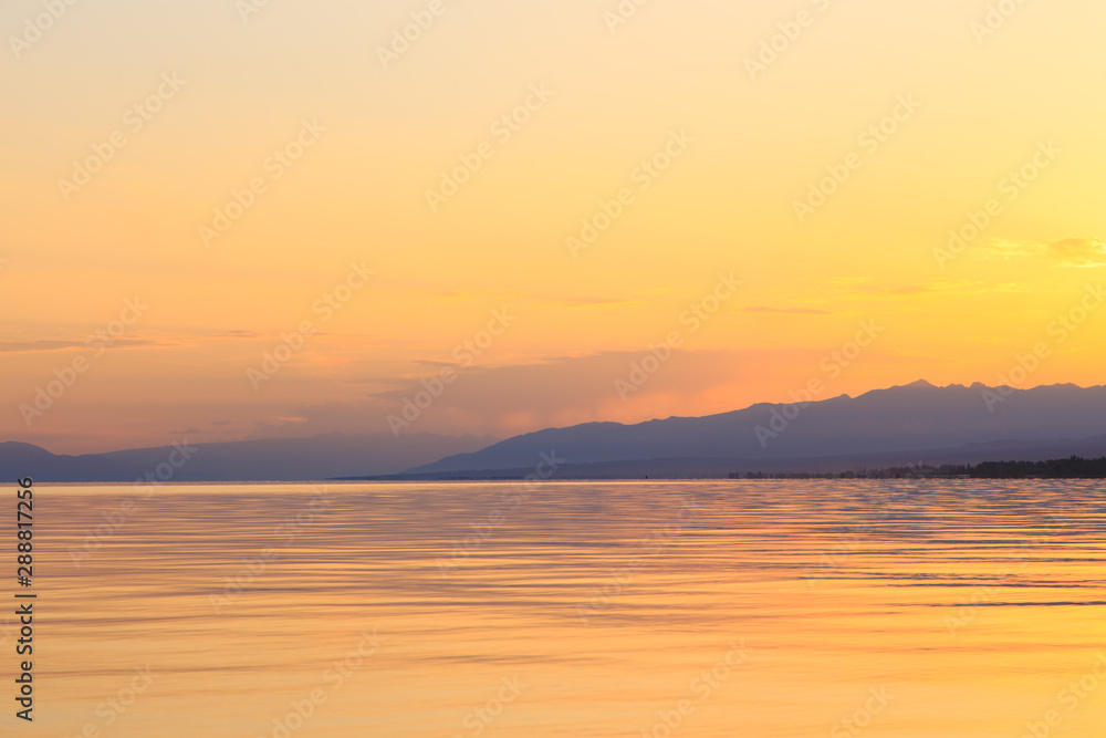 Obraz premium Beautiful sunset on a lake in the mountains. Kyrgyzstan, Issyk-Kul Lake. Bright sky, background in warm colors.