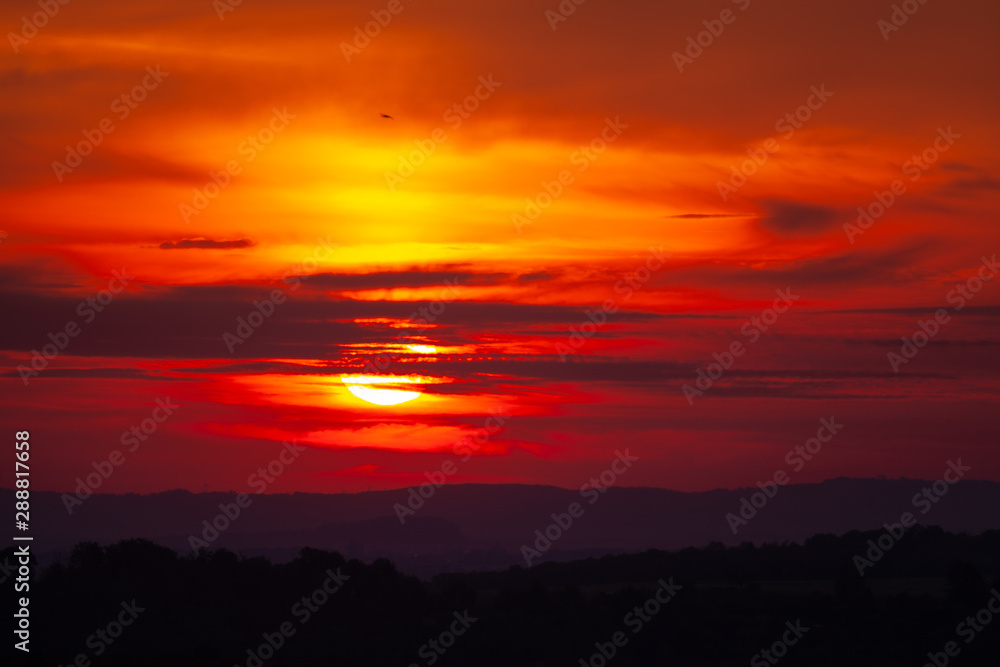 Red sunrise over hills with small wind power plants on horizon