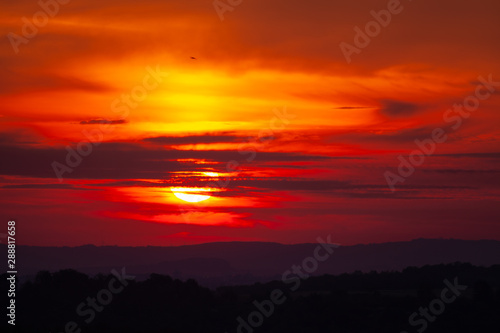 Red sunrise over hills with small wind power plants on horizon