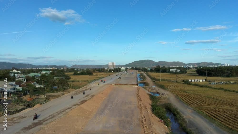 Qui Nhơn is a coastal city in Vietnam known for agriculture and tourism. In this aerial shot the camera flies over farmland and a partially sealed road carrying motor vehicles in the sunny landscape Qui Nhơn is a coastal city in Vietnam known for agriculture and tourism. In this aerial shot the camera flies over farmland and a partially sealed road carrying motor vehicles in the sunny landscape