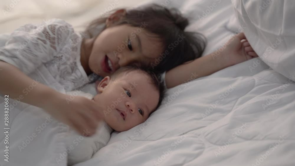 asian daughter kid with infant sibling playing on bed wearing white together asian daughter kid with infant sibling playing on bed wearing white together