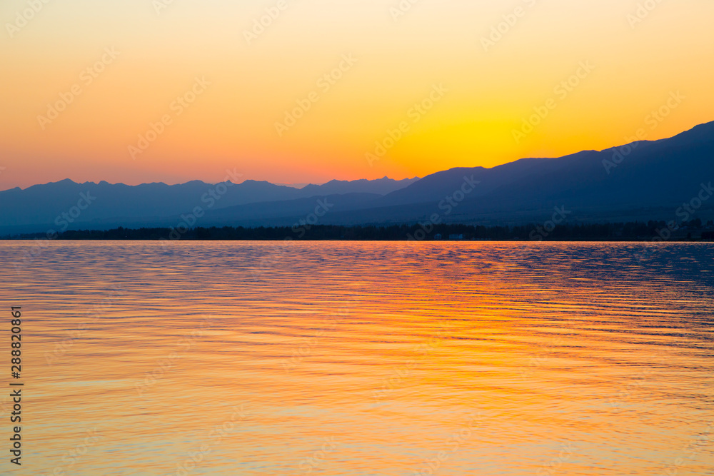 Beautiful sunset on a lake in the mountains. Kyrgyzstan, Issyk-Kul Lake. Bright sky, background in warm colors.