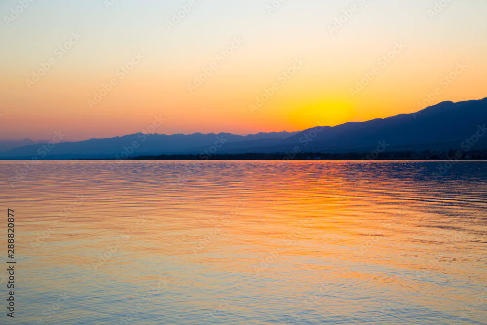 Obraz premium Beautiful sunset on a lake in the mountains. Kyrgyzstan, Issyk-Kul Lake. Bright sky, background in warm colors.