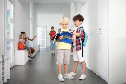 Boys wearing shorts and sneakers standing and reading together