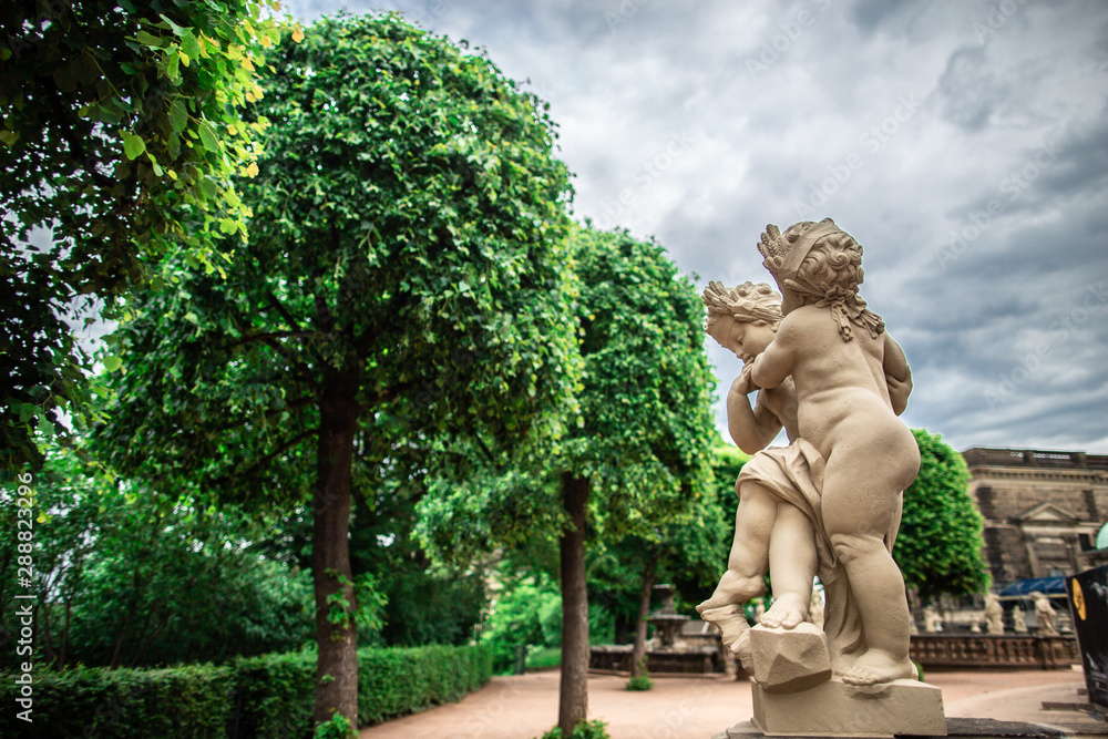 Dresden, Germany - may 27, 2019. Sculpture of small cupids near alley of green trees, Zwinger palace