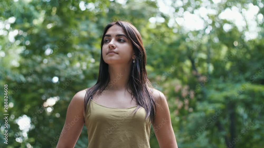 Beautiful girl standing in a green park and looking around in summer in slo-mo Beautiful girl standing in a green park and looking around in summer in slo-mo