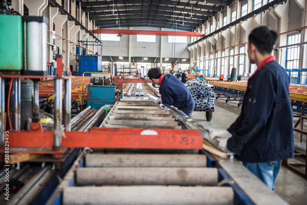Luannan County, Tangshan City, China - October 20, 2016: Mechanical equipment and finished products in the workshop of aluminium alloy products factory, and skilled workers are working. Luannan County, Tangshan City, China - October 20, 2016: Mechanical equipment and finished products in the workshop of aluminium alloy products factory, and skilled workers are working.