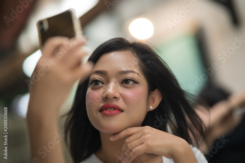 Asian young girl is sitting in the cafe take a selfie using smart-phone