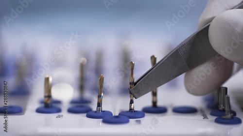 dentist is choosing and taking by tweezers a bor for drilling of teeth in dental office, close-up view