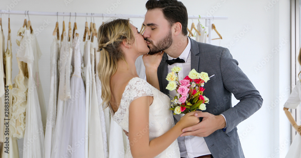 The lovers give flowers to the bride and kissed happy and couple love standing in wedding studio The lovers give flowers to the bride and kissed happy and couple love standing in wedding studio