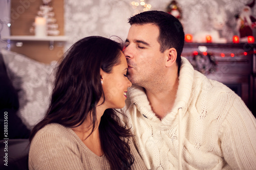 Beautiful young wife kissed on her forehead by her loving husband on christmas