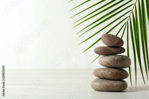 Stack of spa stones and palm leaf on table against white background, space for text