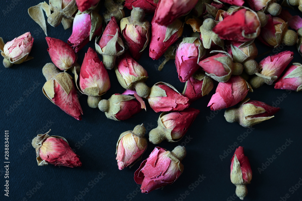 Fototapeta premium Dried rose buds scattered on a dark surface. Rose tea close up