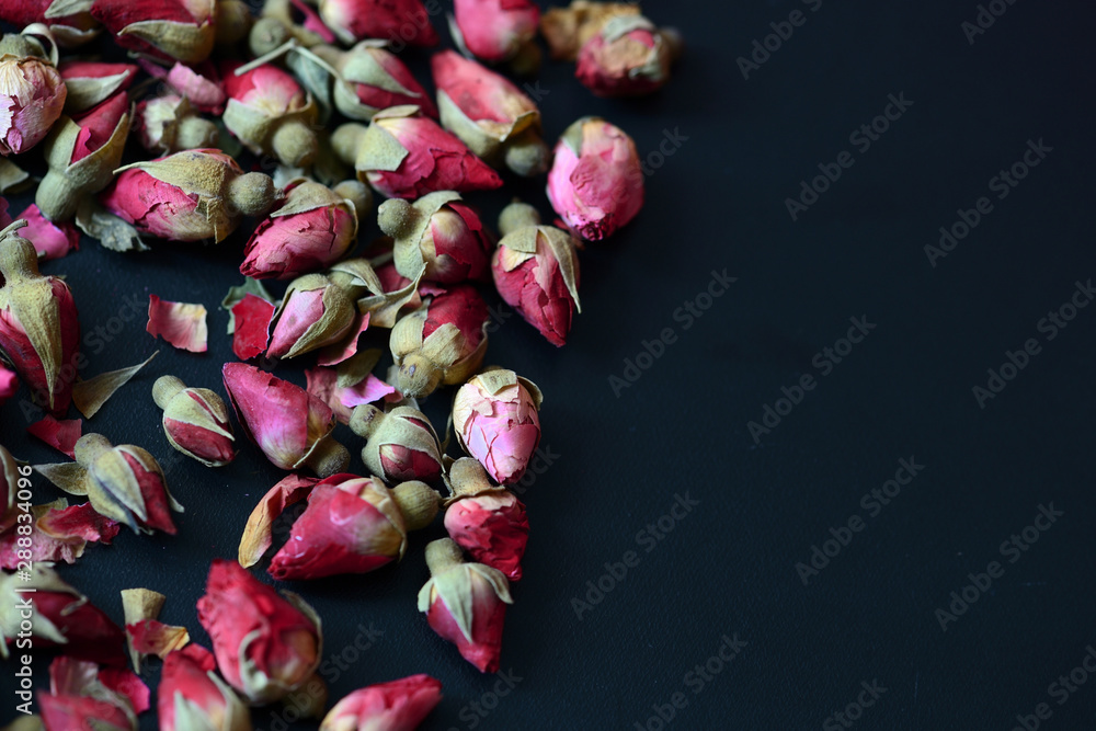Dried rose buds scattered on a dark surface. Rose tea close up