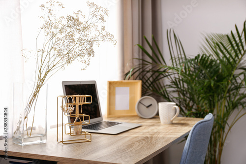 Stylish workplace interior with laptop on wooden table near window