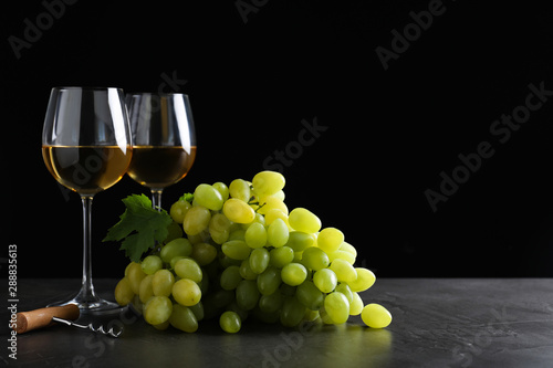 Fresh ripe juicy grapes with wineglasses on grey table against black background, space for text