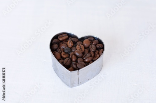 Roasted coffee beans background/ Coffee beans in heart shape at light wooden background/ Coffee background © Sanja