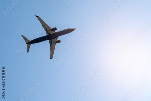 plane flies in blue summer sky against the sun