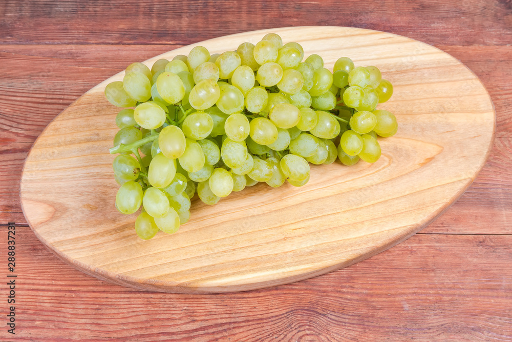 White grapes cluster on the oval wooden serving board White grapes cluster on the oval wooden serving board