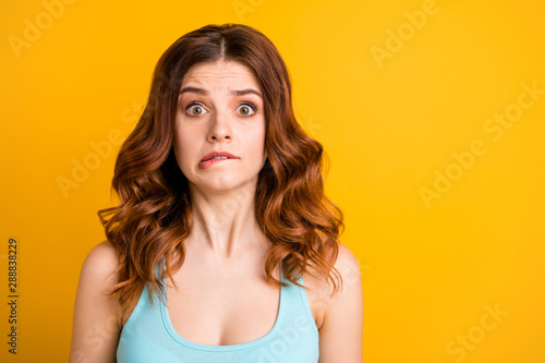 Photo of shocked girlfriend biting her lips because of being worried with something she feels guilty with while wearing teal tank-top isolated with vibrant yellow color background