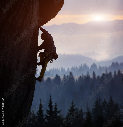Slika na platnu Silhouette of man rock climbing on straight vertical rock at sunrise