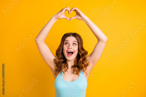 Photo of trendy wavy curly cute nice charming sweet pretty girlfriend being girlish and feminine wearing turquoise singlet showing heart above her head isolated with bright color yellow background