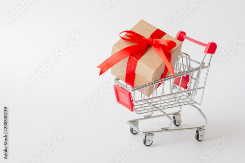 Gift box on miniature shopping cart on white background. Christmas and happy new year concept.