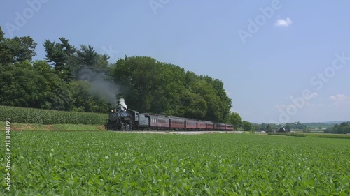 A 1924 Steam Engine with Passenger Train Puffing Smoke Traveling Along the Amish Countryside on a Summer Day photo