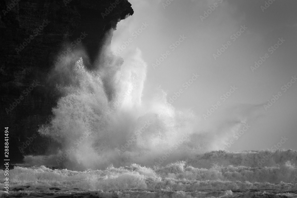 Black and white image of huge waves crashing against the rocks at Piha beach, Waitakere, New Zealand
