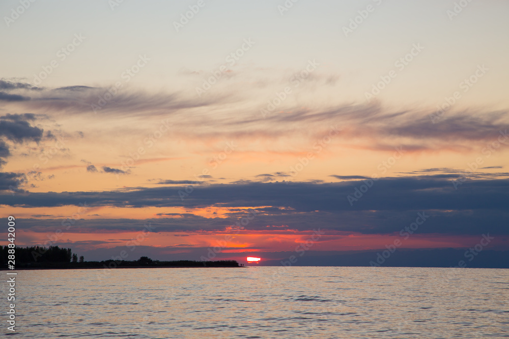 Naklejka premium Beautiful sunset on a lake in the mountains. Kyrgyzstan, Issyk-Kul Lake. Bright sky, background in warm colors.