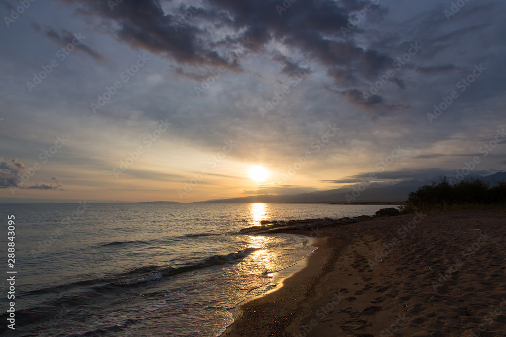 Beautiful sunset on a lake in the mountains. Kyrgyzstan, Issyk-Kul Lake. Bright sky, background in warm colors. Beautiful sunset on a lake in the mountains. Kyrgyzstan, Issyk-Kul Lake. Bright sky, background in warm colors.