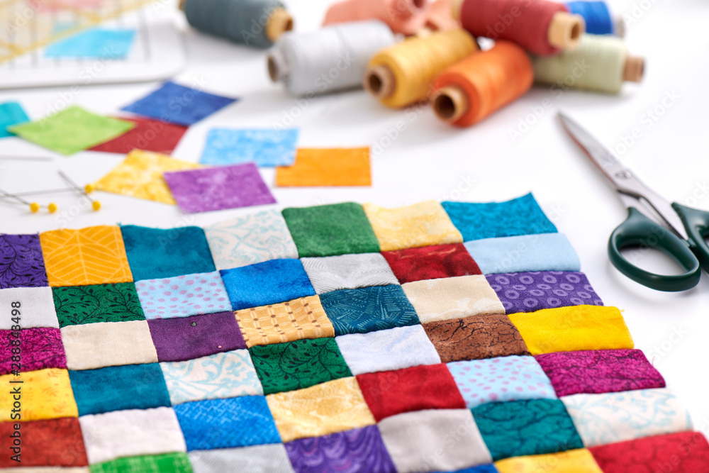 Colorful part of quilt sewn from square pieces, spools of thread, scissors, quilting and sewing accessories - obrazy, fototapety, plakaty 