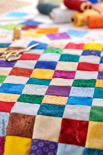 Colorful part of quilt sewn from square pieces, spools of thread,  quilting and sewing accessories