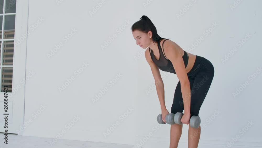 A young athletic woman in a bright apartment performs a deadlift with