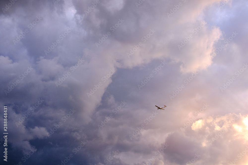 Tiny plane in front of a colorful and cloudy sky in vivid evening athmosphere