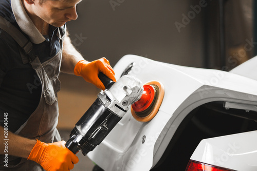 Worker polished white car with orbital polisher in auto repair shop, close-up. Vehicle detailing. photo