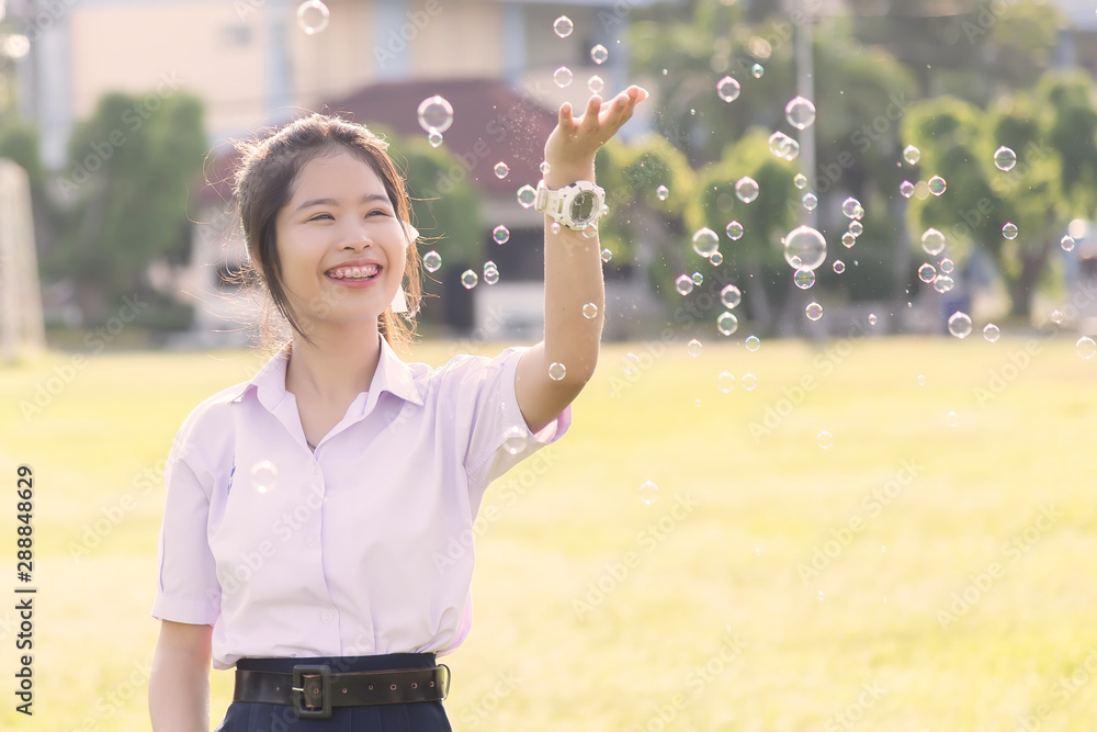 Asian cute girl in a white school uniform is playing a bubble balloon on the lawn. Cute girl is