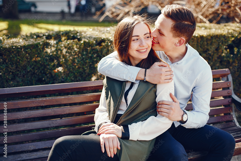 handsome young guy in a blue shirt sitting on a bench in a sunny summer city along with her cute girl in a white shirt