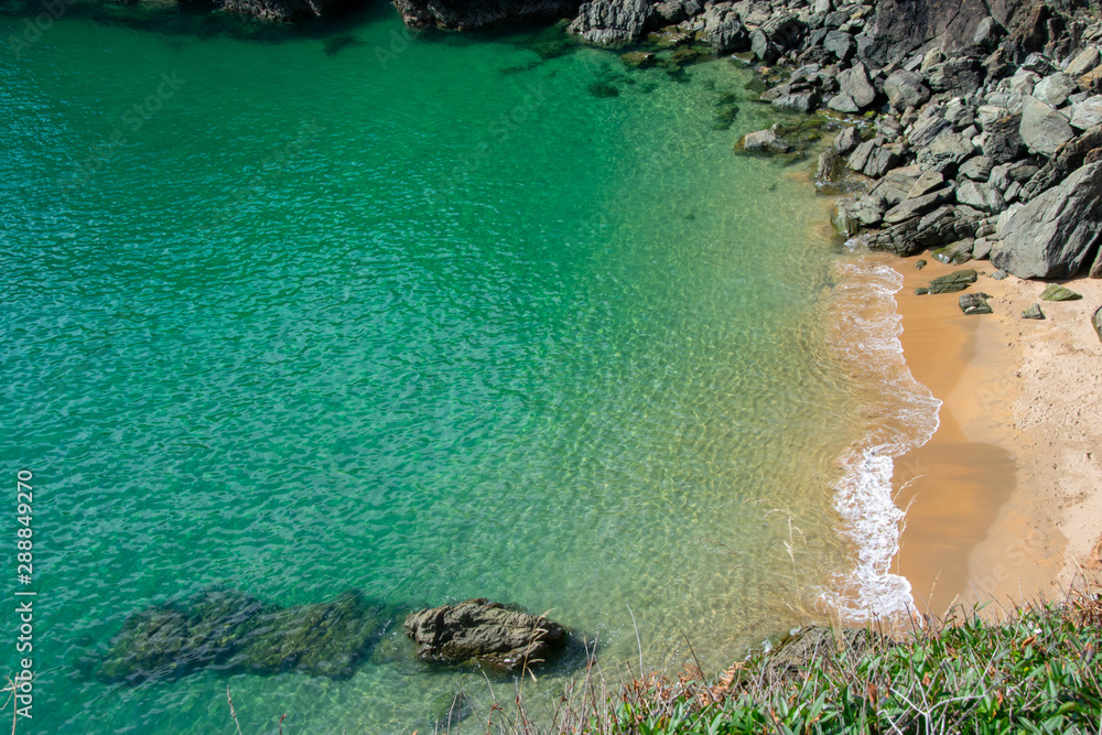 A natural paradise of crystal clear aqua sea with waves breaking on a deserted cove with bright yellow sand near Gara Rock and Moor sand on the Jurassic coast in Devon, United Kingdom