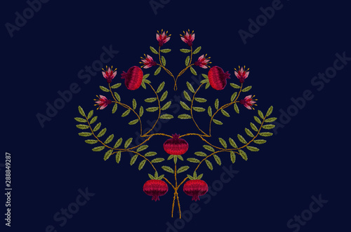 Embroidery satin stitch bouquet of flowers and fruits of red pomegranates on bent twigs with green leaves on dark blue background