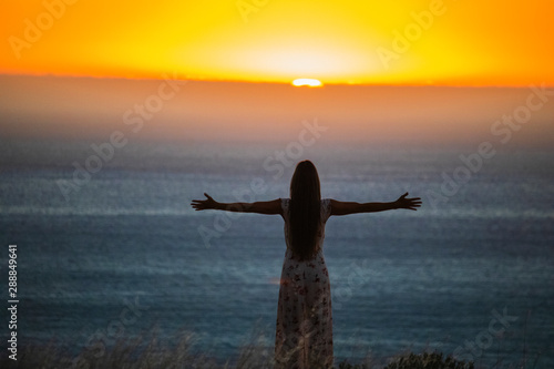 Silhouette of a beautiful woman standing with her arms spread open at sunset or sunrise.