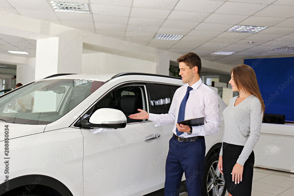 Car dealership sales person at work concept. Portrait of young sales representative wearing formal wear suit, showing vehicles at automobile exhibit center. Close up, copy space, background. Car dealership sales person at work concept. Portrait of young sales representative wearing formal wear suit, showing vehicles at automobile exhibit center. Close up, copy space, background.