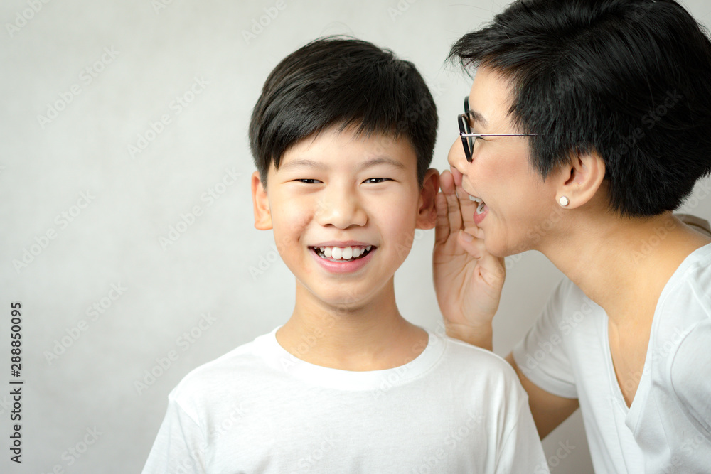 A joyful face of an asian smart looking preteen boy listen to a secret surprise that his mom whispering to his ears. Good news, Parenting teen, Happy family, Preteen boy and mom, Studio portrait. A joyful face of an asian smart looking preteen boy listen to a secret surprise that his mom whispering to his ears. Good news, Parenting teen, Happy family, Preteen boy and mom, Studio portrait.