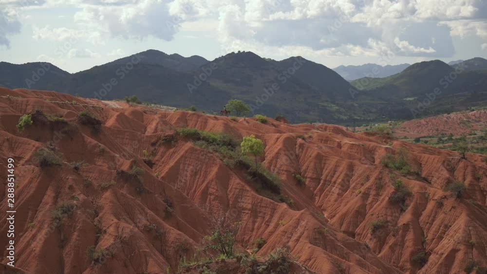 Lonely Man riding a horse in the distance over the empty red terra rossa mountains of the Mixteca Alta UNESCO global geopark in Oaxaca Mexico.